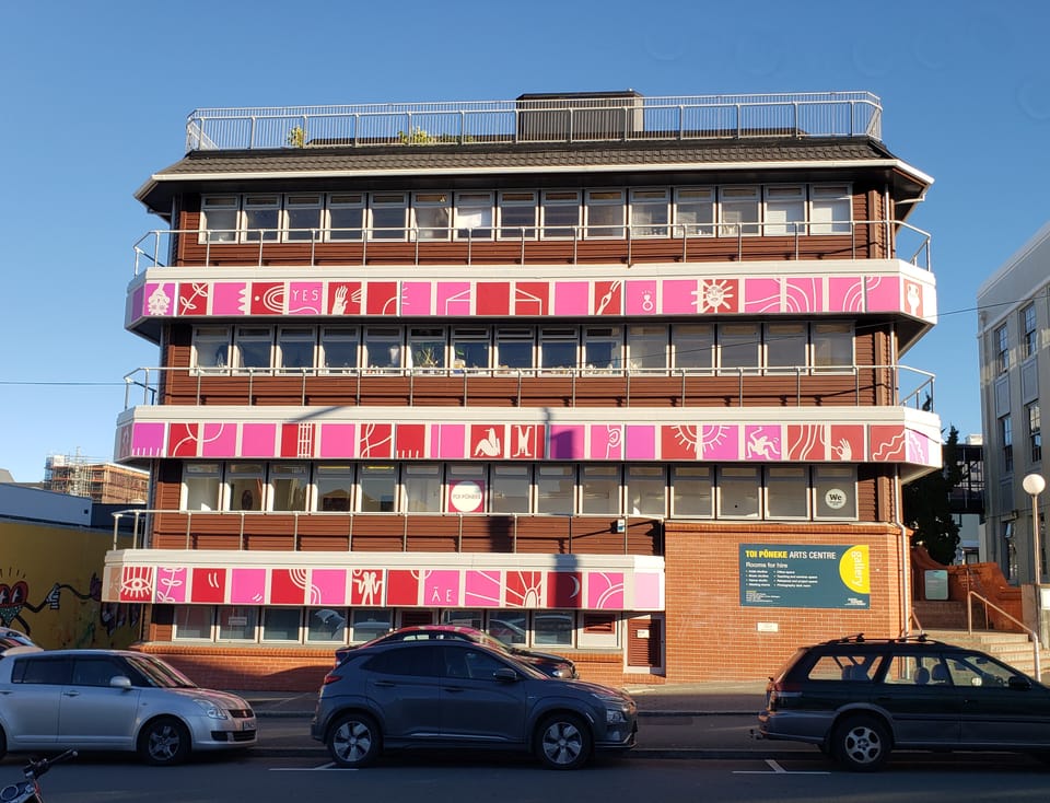 Toi Pōneke - a 4 storey arts centre mostly made of brick, with pink and red art around the outsides